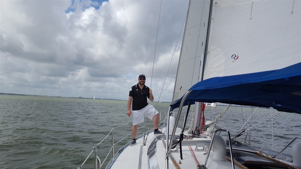 Man posing at the bow of a sailboat on the water.
