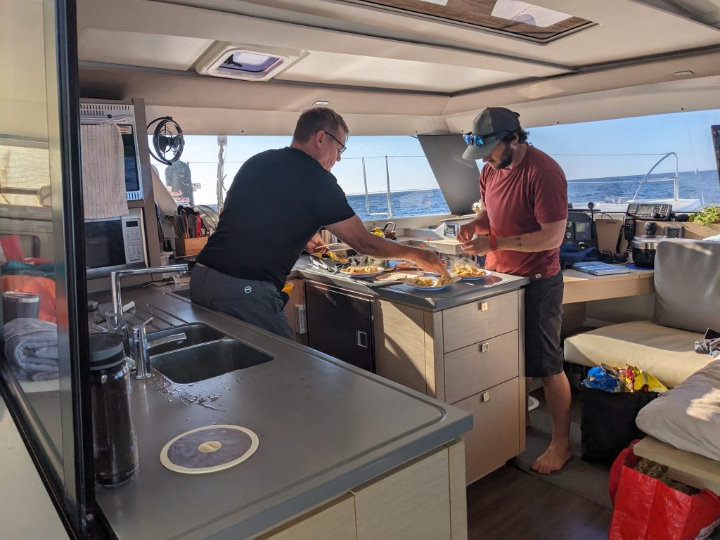 Image of two men preparing plates of food in the galley of a boat.