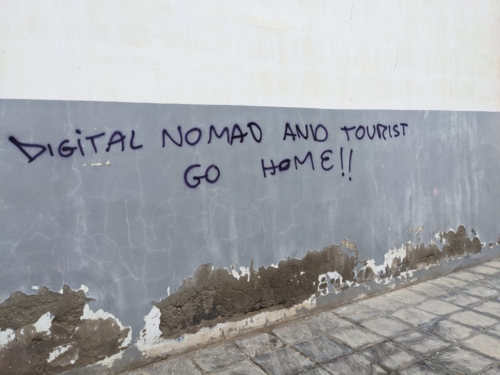 Image of a wall with graffiti reading "DIGITAL NOMAD AND TOURIST GO HOME!!"