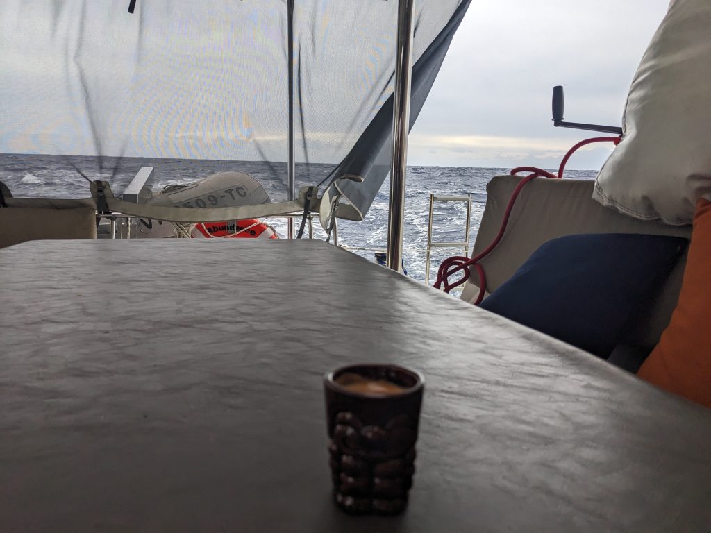 Imnage of a cup of espresso sitting on a table of a boat wohich is underway at sea.