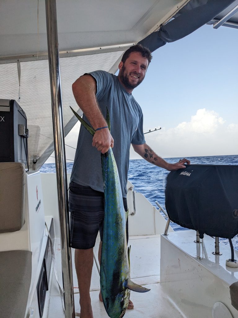 Image of a man holding a mahi-mahi fish by the tail the fish is as tall as the man