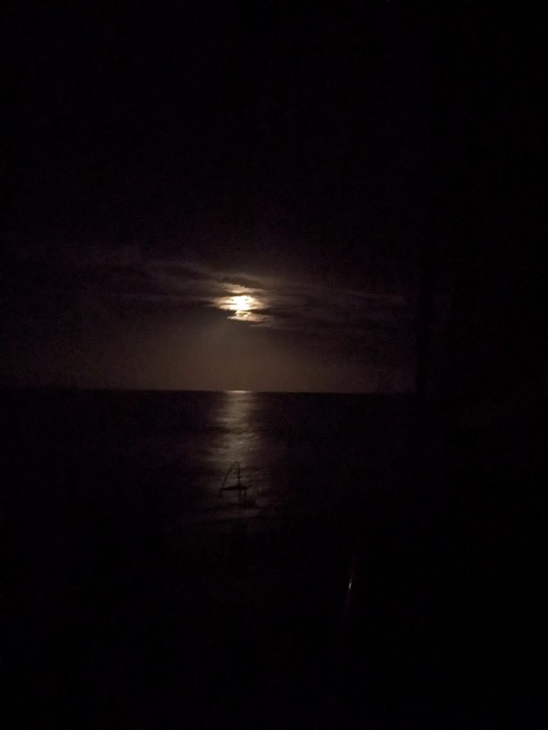 Image of the sky with the moon hidden behind clouds, with the horizon of the sea