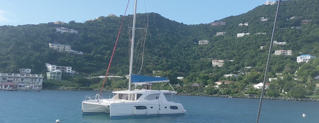 Image of sailing catamaran moored offshore, with green foothills in the background.