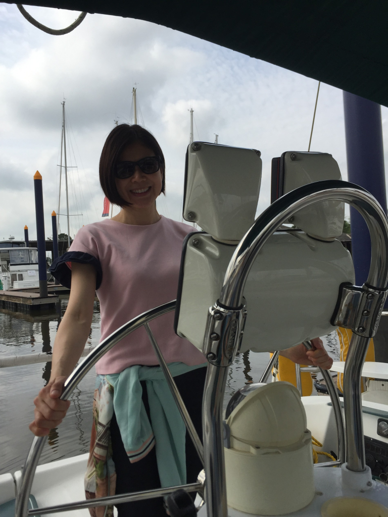 Image of awoman behind the wheel on a boat moored in a marina