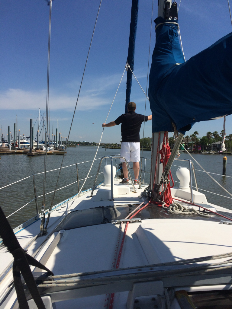 Image of man at the bow of a sailboat leaving the marina