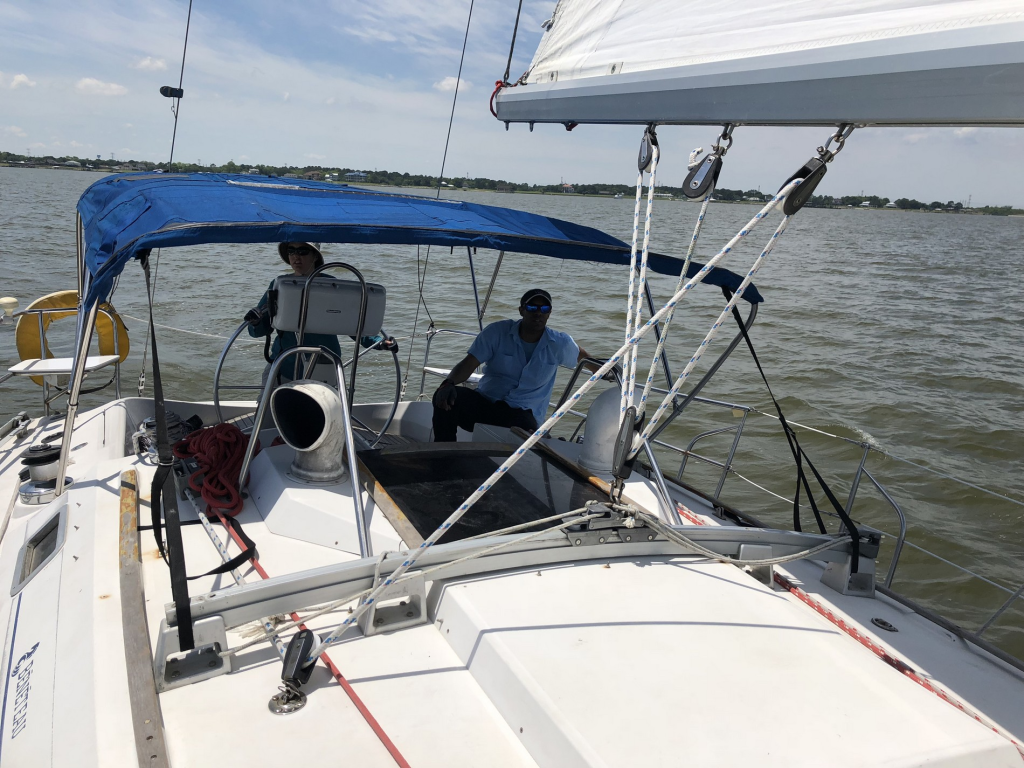 Image of 2-person crew at the helm of a sailboat under way