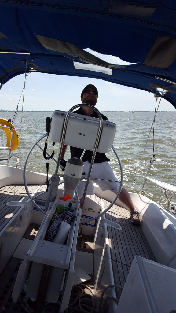 Image of a man at the helm of a sailboat, sailboat heeled over, man looking up at the sails
