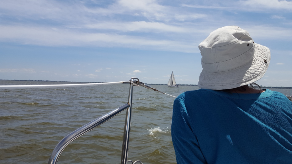 Image of a woman seated on a boat looking out at other sailboats in the distance.