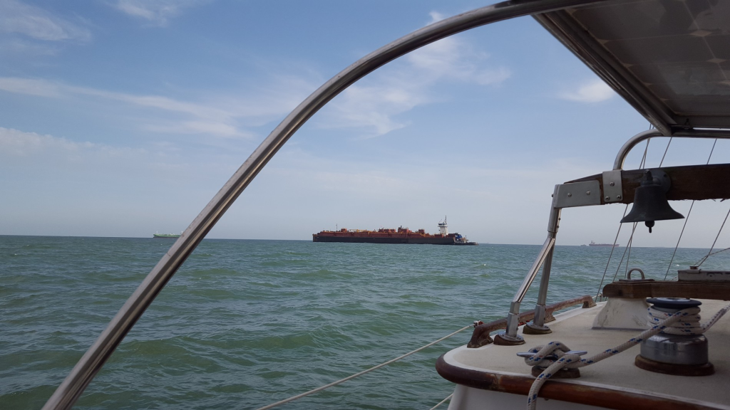 Image of the sea taken from a boat with a cargo freighter in the distance