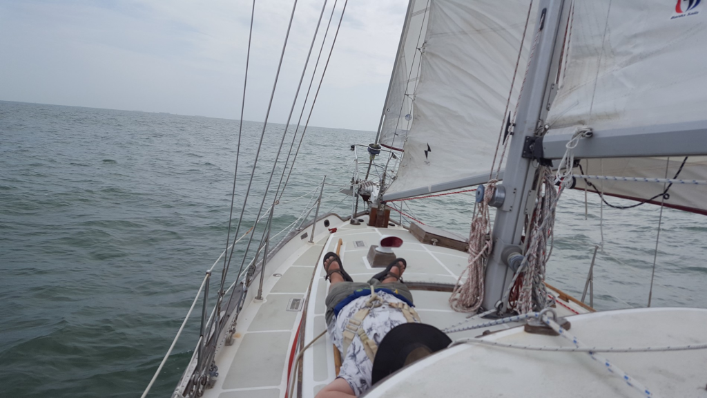 Image of a man lounging on the deck of a sailboat, lying on his back apparently taking a nap
