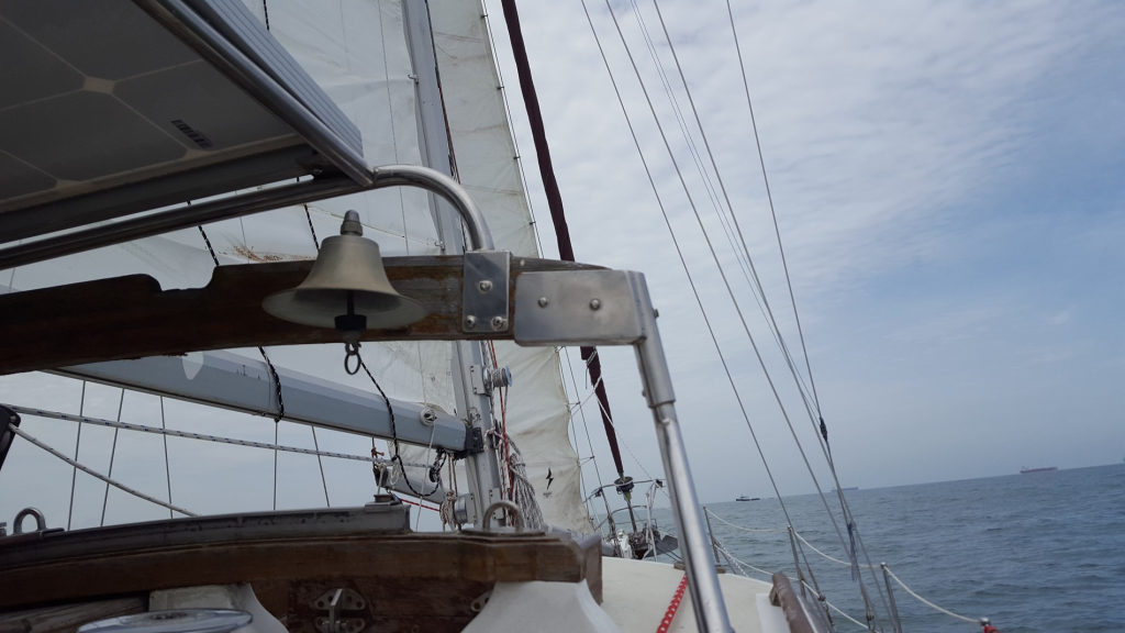 Image of a sailboat at sera, focusing on a bell which is mounted on a wooden cross-beam above the main cabin.