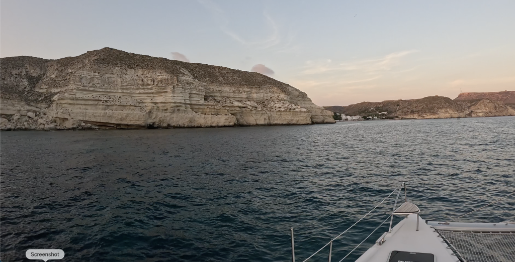 Inage of a small hill on the coast, taken from aboard a catamaran which is in the ocean.