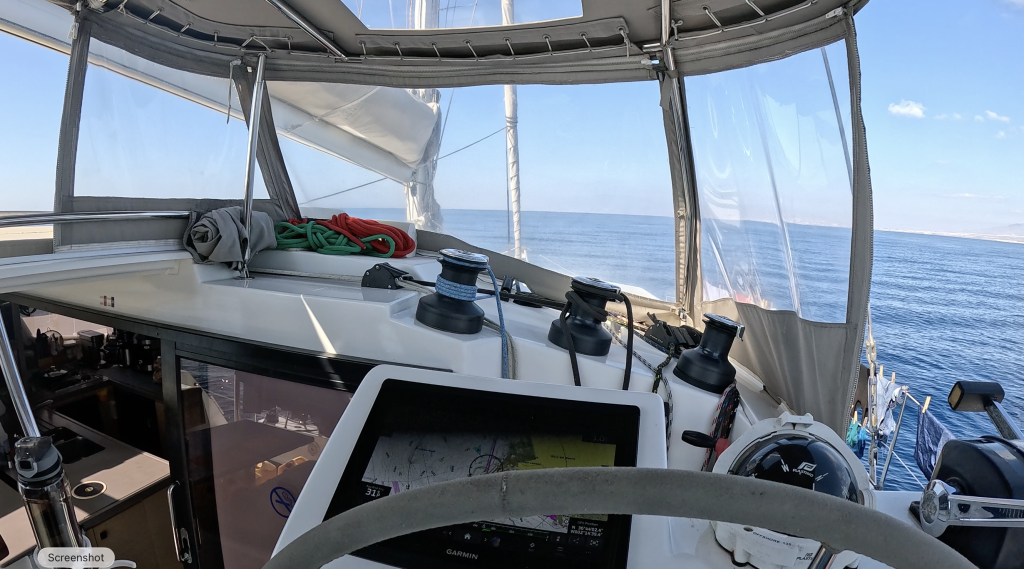 Image takenb from the cockopit of a sailing catamaran, with the steering wheel, GPS, and sea visible.